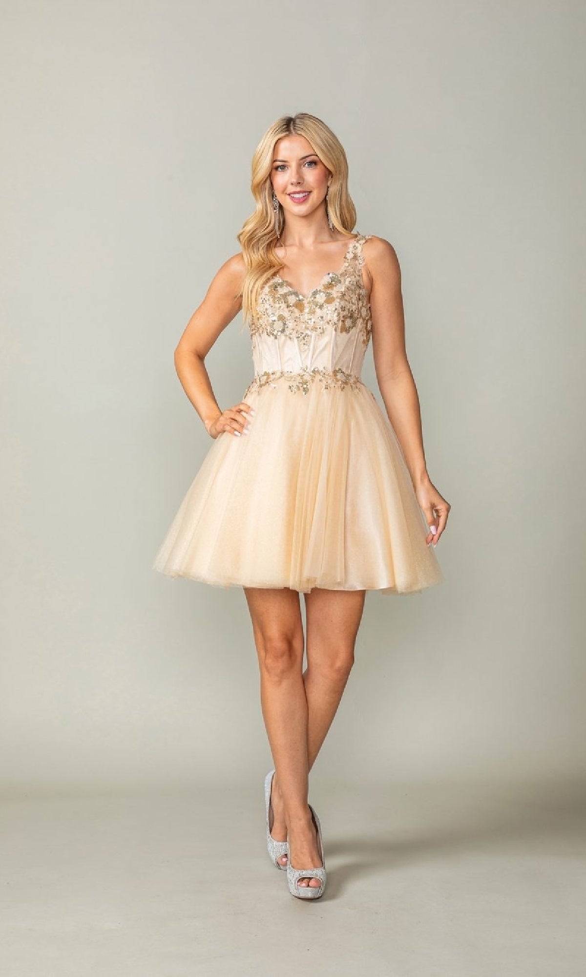Woman wearing a short champagne dress with floral embellishments on a plain background